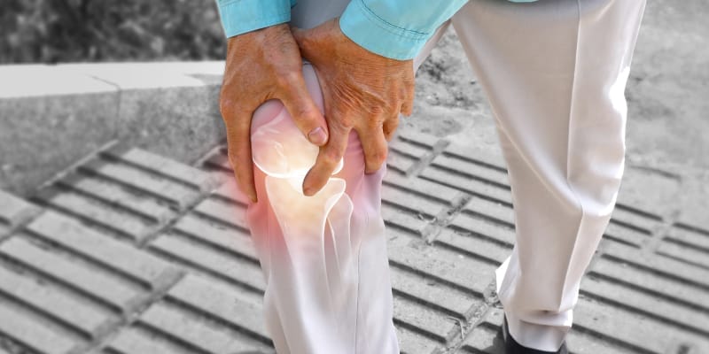 An elderly man holds his painful knee, showing signs that may lead to knee surgery.