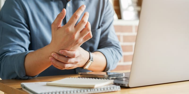A man holding a wrist due to pain while working on a laptop