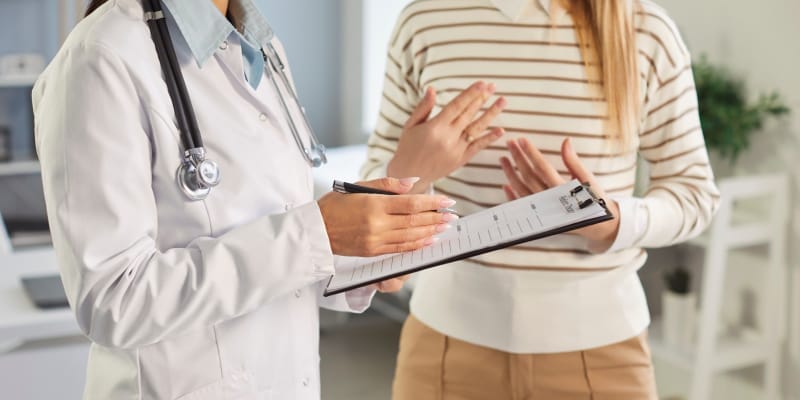 A Woman doctor noting down the health history of a patient on paper.